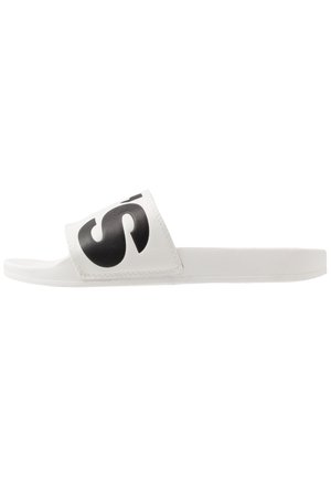 Sandalia blanca de playa con una correa ancha que presenta un gran logo negro. Material suave, suela plana, diseño minimalista y textura lisa.