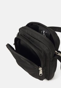 Melns neilona plecu soma ar vairākiem rāvējslēdzējiem un strukturētu virsmu. Iekšpusē ir Calvin Klein logo tag.