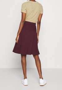 Bordowa spódnica typu skater o rozkloszowanym fasonie, miękka w dotyku, zestawiona z biało-żółtą bluzką z krótkim rękawem w paski. Całość uzupełniają białe sneakersy.