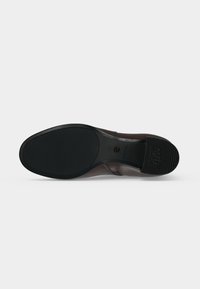 Semelle de chaussure avec une surface en caoutchouc noir texturé, une partie de la voûte plantaire lisse et "ANTI SLIP" embossé sur la zone du talon.
