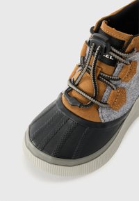 Brune og grå joggesko med en teksturert gummisåle, elastiske snørebånd, mykt stoff øvre, og en grå tåhette med vertikale spor.