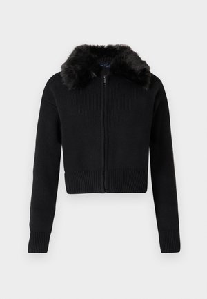 Melns nedaudz īsāks džemperis ar rāvējslēdzi priekšpusē un ribota auduma struktūru. Aprīkots ar mākslīgās kažokādas apkakli un garām piedurknēm. Vienkāršs, mūsdienīgs dizains.