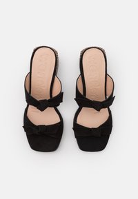 Černé semišové slip-on boty se čtveratou špičkou, s dvěma mašlemi jako ozdobou. Vložka je v jemně béžové barvě s embosovaným logem.