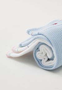 Fire sokker rullet sammen: en lys blå, to hvite med fargede detaljer på mansjettene, med ribbet tekstur og små broderte detaljer.