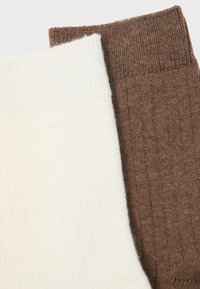 Dva para rebrastih čarapa, jedan u bijeloj i jedan u tamnosmešnoj boji, prikazujući teksturirani pleteni uzorak s elastičnim otvorima.