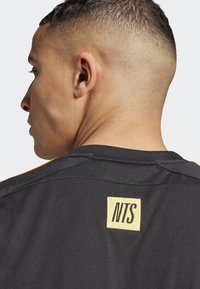 Black sports jersey with orange accents; features a gold "NTS" label on the back neck area; textured fabric with a comfortable fit.
