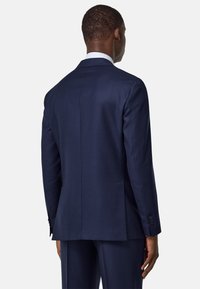 Veste de costume marine en tissu lisse, dotée d'une fente arrière, de deux boutons et d'une coupe ajustée. Design sobre avec un minimum de détails.