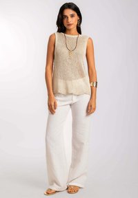 Haut sans manches beige en tricot avec un ourlet légèrement festonné, associé à un pantacourt en lin blanc ample. Collier en bois décoratif et accents dorés.
