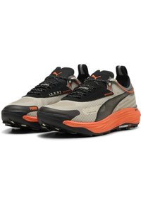 Scarpe da corsa leggere con una tomaia in rete beige, accenti neri e dettagli arancioni. Presentano una suola testurizzata per aderenza e stabilità.