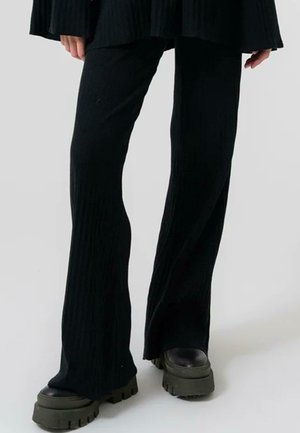 Pantalons évasés noirs à côtes avec une finition texturée. Assortis à des chaussures à plateforme noires, épaisses avec une semelle massive.