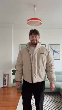 Casaco puffer bege com gola alta, fecho frontal e um bolso no peito. Feito de tecido brilhante, apresenta um corte descontraído e costuras robustas.