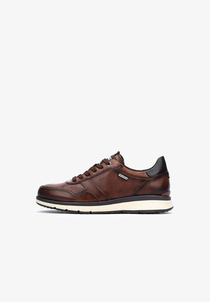 Zapatilla de cuero marrón con textura perforada, acentos negros y suela media blanca. Cuenta con cordones y un logo. Diseño atlético clásico.