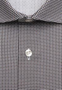 Gros plan d'une chemise à motifs marron et blanc avec col pointu et un seul bouton blanc visible.