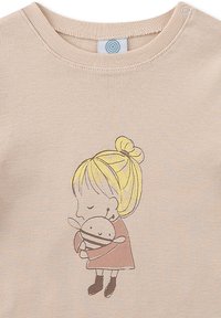 Hellbeige, Baumwoll-T-Shirt mit Rundhalsausschnitt und kurzen Ärmeln, das eine gedruckte Illustration eines Mädchens zeigt, das eine Puppe umarmt.