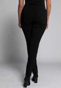 Pantaloni neri attillati con una texture liscia, vita alta e caviglie affusolate, abbinati a scarpe nere con tacco a blocco.