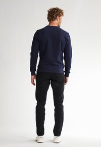 Felpa navy con maniche lunghe, scollo a girocollo e polsini a costine, abbinata a jeans neri slim-fit e sneaker bianche.