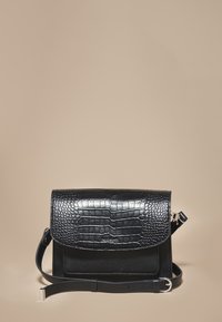 Czarna skórzana torebka z teksturowanym wzorem krokodyla na klapie, o prostokątnym kształcie i regulowanym pasku.