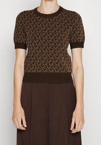 Camisa de punto marrón con un diseño de patrón geométrico en marrón claro, mangas cortas acampanadas y un cuello redondo y dobladillo acanalados.