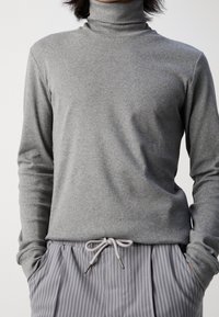 Grauer Rollkragenpullover aus weichem Material, mit langen Ärmeln und lockerer Passform. Kombiniert mit gestreiften grauen Jogginghosen mit Kordelzug.