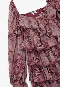 Blusa arrugada en rosa apagado con intrincados patrones florales y de cachemira. Tela transparente con mangas abullonadas y puños elásticos.