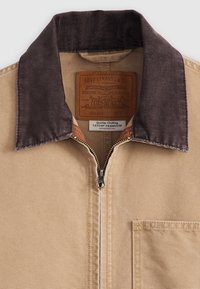 Hnědá bunda s tmavě hnědým manšestrovým límcem, předním zipem, kapsou na hrudi a štítky Levi Strauss & Co. uvnitř límce.