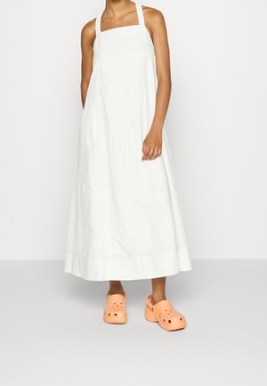 Robe maxi blanche sans manches avec un décolleté carré et des coutures verticales. Assortie avec des sabots orange dotés de trous de ventilation.