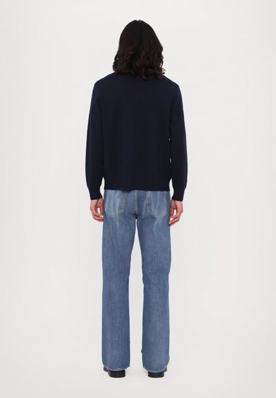 Sweater azul-marinho com decote redondo, punhos canelados, combinado com jeans claros de cintura alta e boca de sino, com bolsos traseiros.