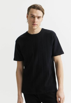 Czarny t-shirt z krótkim rękawem o prążkowanej teksturze i pionowych paskach, z okrągłym dekoltem i luźnym krojem.