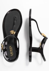 Svarta lackläderssandaler med en flip-flop design, som har en guldig logotypdetalj och en elegant klack för en modern silhuett.