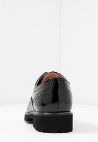Czarne lakierowane buty skórzane z detalami brogue, okrągłym noskiem i grubą czarną podeszwą. Posiadają gładką strukturę z kontrastującymi wycięciami.