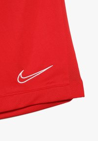 Pantalones cortos deportivos rojos con un logo de swoosh blanco de Nike cerca do la parte inferior y paneles de tela de malla a los lados.
