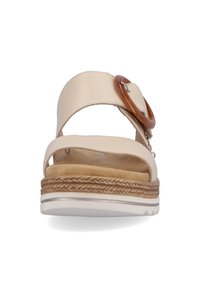 Beige Sandale mit einem breiten Riemen, ausgestattet mit einer runden Holzschnalle. Weiche Innensohle, geflochtene Textur auf der Plattform und weiße Außensohle.