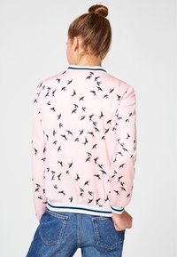 Světle růžová bomber bunda s černým potiskem ptáků, s ribbenovým límcem a manžetami. Hladká tkanina s přiléhavým střihem a elastickým spodním lemem.