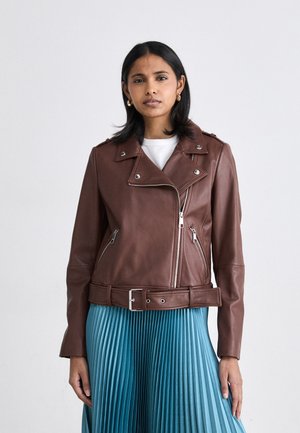 Brown leather motorcycle jacket with silver hardware, zippered pockets, and a belted waist, paired with a pleated turquoise skirt.