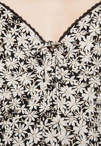 Un tissu noir orné de motifs de marguerites blanches. Présente un col en V avec une bordure en dentelle et un détail de nœud au centre.