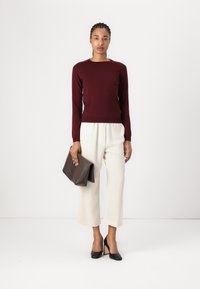 Bordeaux langærmet sweater parret med cremefarvede vidde bukser og sorte høje hæle. Holder en brun clutch. Simpelt, moderne design.