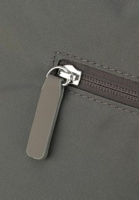Primo piano di una borsa in tessuto grigio dotata di chiusura a zip con un tirazip in argento e una superficie texturizzata. Cuciture visibili lungo il bordo.