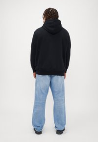 Svart huva tröja med mjuk textur, tillsammans med ljusblå vida jeans och svarta sneakers. Synlig sömnadsdetalj.