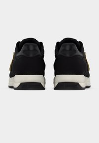 Ασπρόμαυρα sneakers Love Moschino, εμφανιζόμενα από πίσω με μαύρες λεπτομέρειες στη φτέρνα και χοντρές λευκές σόλες σε απλό φόντο.