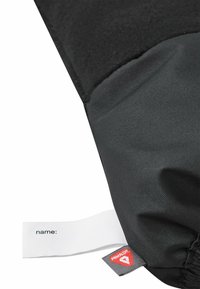 Schwarzer Stoff mit strukturierter Oberfläche, versehen mit einem weißen Etikett mit "Name:" und einem rot-weißen Logoschild in der unteren Ecke.