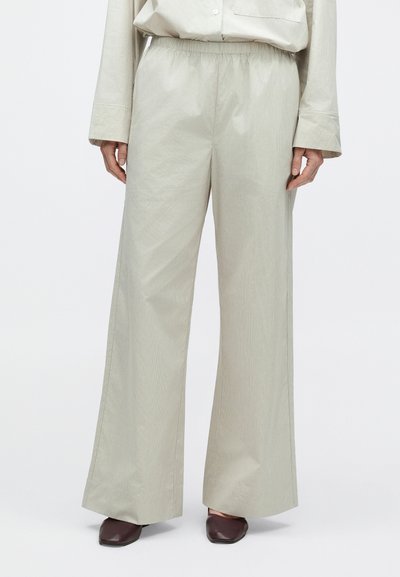 Pantalon gris clair à jambes larges avec une taille élastique, tissu texturé et coupe droite. Associé à des chaussures marron foncé à bout pointu.