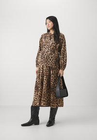 Kjole i leopardmønster med løs passform, lange ermer og høy nakke, kombinert med svarte knelang støvler og en svart håndveske.