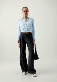 Camicia blu chiaro a maniche corte, pantaloni neri a vita alta con pieghe, borsa nera e sneakers bianche e nere. Accessori semplici.