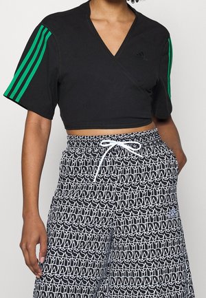 Top envolvente negro de manga corta con detalle de tres franjas verdes. Combinado con pantalones sueltos blancos y negros con un estampado y una cinturilla ajustable.