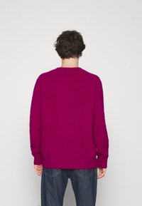 Maglione fitted a scollo rotondo di colore magenta brillante, realizzato in tessuto testurizzato con polsini e orlo a costine. Sul retro presenta un piccolo logo all'altezza del collo.