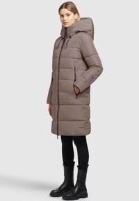 Parka imbottita marrone con cappuccio, dotata di zip frontale, tasche laterali e dettagli elasticizzati. Si abbina perfettamente a leggings neri e stivali chunky.