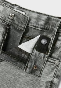 Grå denimjeans har en dragkedja med knappstängning och en doldt ficka med vitt foder. Tyget har en texturerad yta.