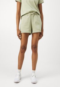 Calções de algodão verde claro, com cintura elástica ajustável, corte descontraído e costuras laterais. Usados com sapatilhas brancas e meias de cano curto.