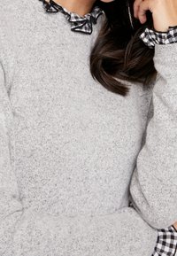Grauer Strickpullover mit einem gerafften Kragen und Manschetten aus schwarz-weißem Vichy-Karo, aus weichem, strukturiertem Stoff und lässiger Passform.