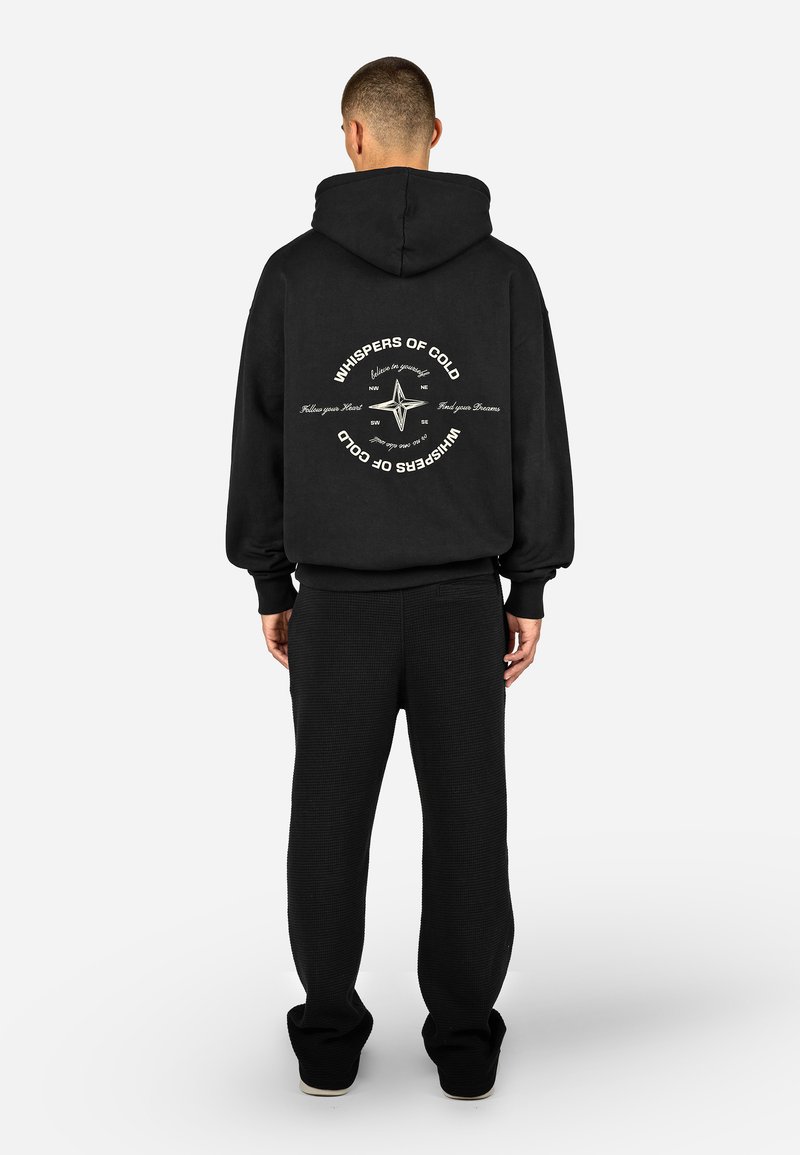 Μαύρη hoodie με κουκούλα και κορδόνι, με εκτυπωμένο σχέδιο πυξίδας στην πλάτη. Συνδυασμένη με μαύρες υφασμάτινες joggers που ταιριάζουν.